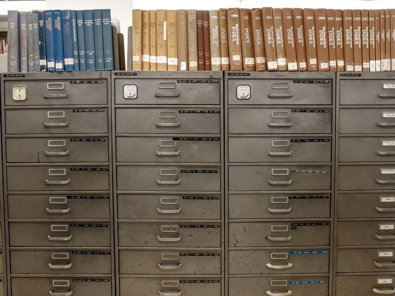 A row of filing cabinets dissolving into pixels, each drawer labelled with a different people-search site logo silhouette.