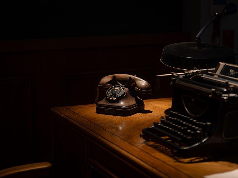 An older landline phone on a kitchen table next to a hand-written note that reads "ask the safe word" with a coffee mug beside it.