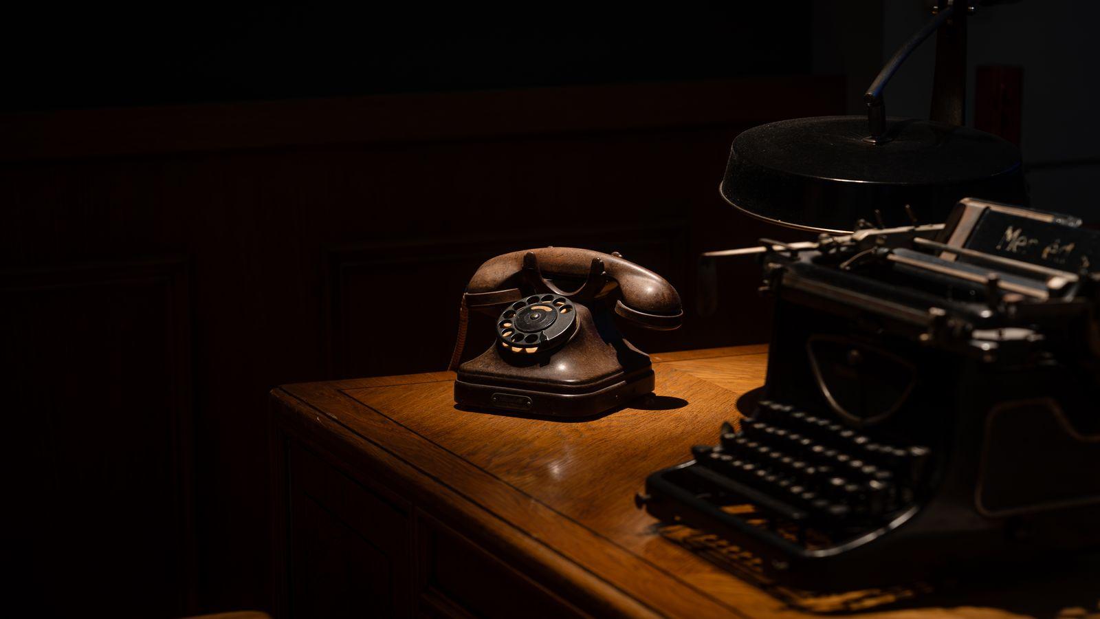 An older landline phone on a kitchen table next to a hand-written note that reads "ask the safe word" with a coffee mug beside it.