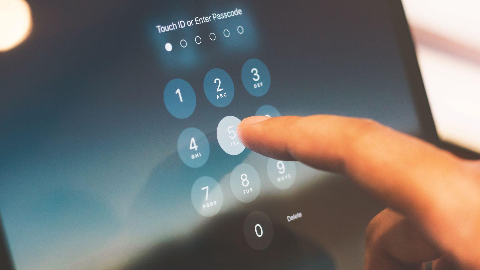 A laptop and a phone on a wooden desk, the phone screen showing a fingerprint prompt and the laptop showing a sign-in page mid-handshake.