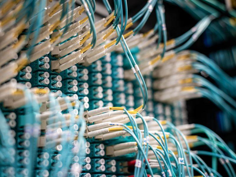 A long-exposure photograph of server room cables glowing pale blue, with a single fibre strand pulled taut across the frame.