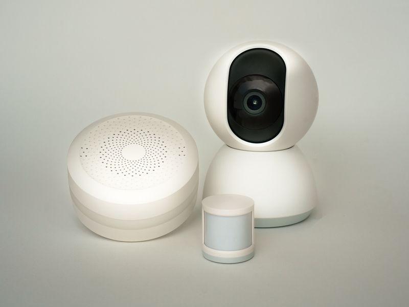 A smart speaker, a thermostat, and a security camera arranged on a wooden table.