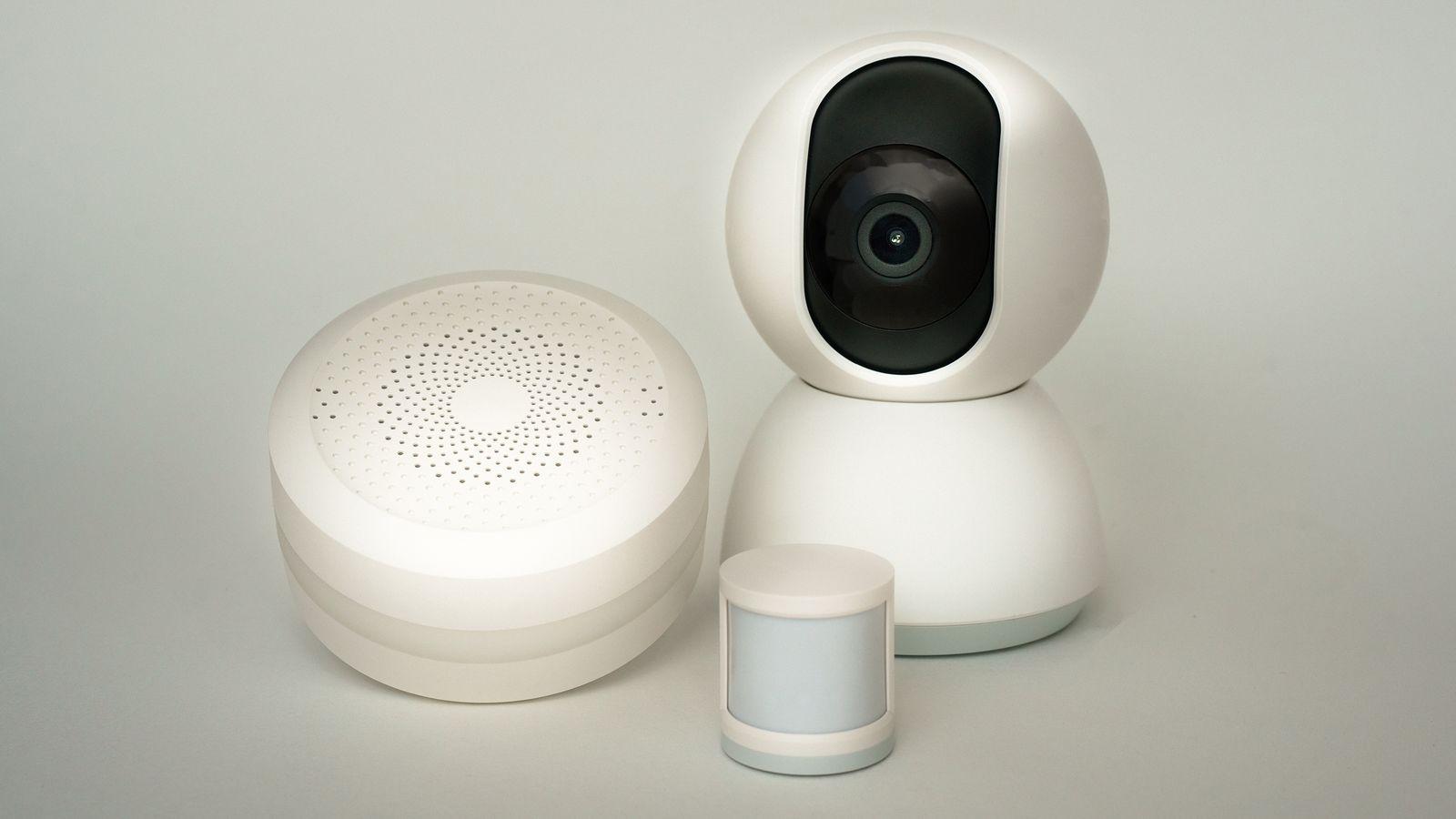 A smart speaker, a thermostat, and a security camera arranged on a wooden table.